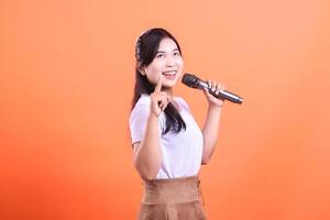 A young woman singing with a microphone, she is smiling and looks excited and joyful during her performance. isolated on orange background photo