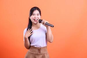 A smiling young Asian woman singing passionately into a microphone. She is happy and expressive, enjoying the performance isolated on orange background photo