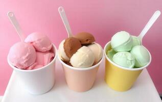 Three cups of ice cream with spoons on a pink background photo