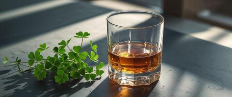 Golden whiskey in a glass next to fresh green clovers on a dark surface. photo