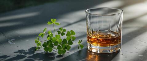 Golden whiskey in a glass next to fresh green clovers on a dark surface photo