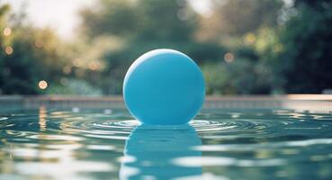 Blue inflatable ball floating in calm swimming pool water during sunny day with reflections on surface and blurred background of garden. photo