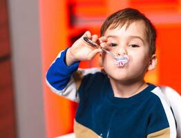 Child enjoying dessert with a spoon. A young boy smiles while playfully holding a spoon with dessert in his mouth, highlighting his joy. photo
