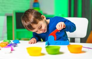 Child plays creatively with toys. A young boy in a blue shirt focuses on crafting with a toy while surrounded by colorful bowls and playful materials. photo