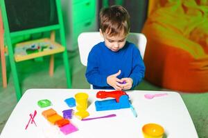 Child plays with bright clay. Child engages in creative play with modeling clay at a table, surrounded by vibrant colors and playful tools. photo