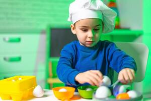 Young chef prepares colorful egg dishes. A child wearing a chef hat carefully arranges different colored eggs in bowls while cooking indoors. photo