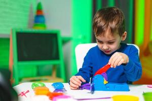 Kid molds bright clay shapes. Young boy enjoys creative activity with bright modeling clay at a brightly lit table filled with tools and clay shapes. photo