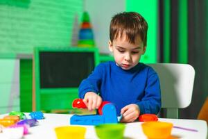 Child playing at a bright table. A young boy engages in playful activity with colorful toy tools and materials in a bright, cheerful room. photo