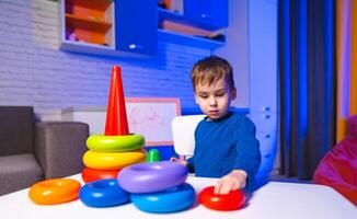 Child playing with stacking toys indoors. A young boy is engaged in stacking colorful toys on a table in a cozy indoor space lit with soft blue hues. photo