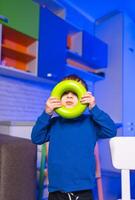 Child playing with a colorful toy ring. A young child holds a bright green ring in front of their face, enjoying playful moments in a colorful space. photo