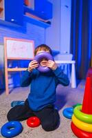 Child stacks colorful toys inside. A young child enjoys stacking colorful toys on a carpeted floor in a cozy, softly lit room. photo