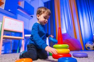 Child stacking colorful blocks. A young boy is playing with colorful stacking rings in a bright, playful room filled with toys and soft furnishings. photo
