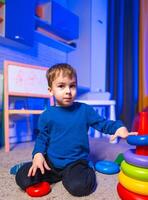 Child with stacking toys. A young child sits on a soft carpet, stacking colorful toys in a bright room with blue lighting. photo