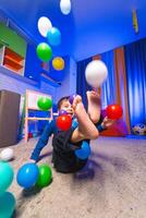 Child enjoys colorful ball play indoors. A joyful child plays with colorful balls in a bright indoor space while relaxing on a soft carpet. photo