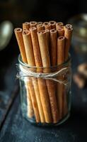 Cinnamon sticks arranged in a glass jar. A rustic glass jar filled with numerous cinnamon sticks tied with twine, accentuating the warm, earthy tones. photo