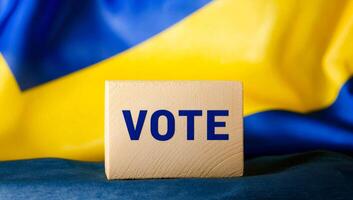 Vote block by Ukrainian flag. A wooden block with VOTE written on it is displayed in front of a Ukrainian flag, symbolizing civic engagement. photo