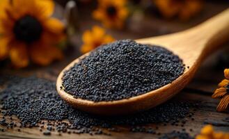 Poppy seeds on wooden spoon with flowers. A wooden spoon filled with black poppy seeds rests on a rustic wooden surface, surrounded by yellow flowers. photo