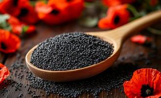 Black seeds and bright flowers. A wooden spoon holds black poppy seeds surrounded by bright red poppy flowers on a rustic wooden surface. photo
