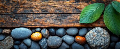Stones and leaves on wood. Smooth stones in various shapes and colors are arranged alongside fresh green leaves on an aged wooden surface. photo