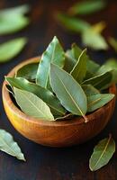 Bay leaves in a wooden bowl on a table. Fresh bay leaves arranged in a natural wooden bowl, resting on a dark wooden table surrounded by scattered leaves. photo