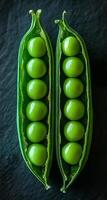 Green peas in pods on dark. Two open pea pods reveal plump green peas nestled inside against a dark background. photo