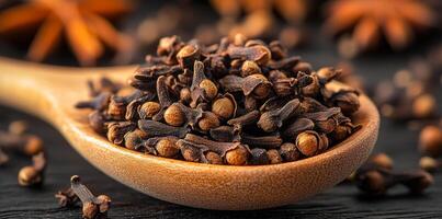 Cloves on wooden spoon, dark. Whole cloves are displayed in a wooden spoon on a dark surface, highlighting their rich color and texture. photo