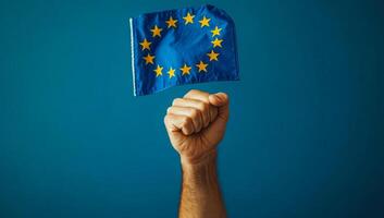 Holding up a European flag in enthusiasm. A hand enthusiastically raises a European flag against a blue background, symbolizing unity and pride. photo