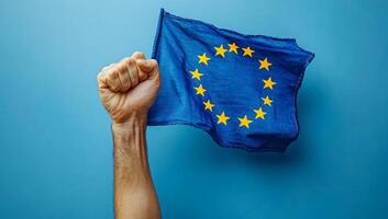 EU flag raised in support. A hand holding the European Union flag high against a blue background, symbolizing unity and pride for the EU. photo
