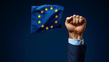 European unity symbolized by raised fist. A hand with a clenched fist holds the European flag against a dark backdrop, representing solidarity and unity. photo
