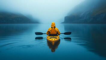 Yellow kayak in misty waters. A person in a yellow kayak paddles through calm, fog-covered waters surrounded by cliffs on a quiet morning. photo