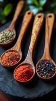 Four wooden spoons with different colored spices on a black surface. The spoons are arranged in a row, with the first spoon on the left and the last spoon on the right photo