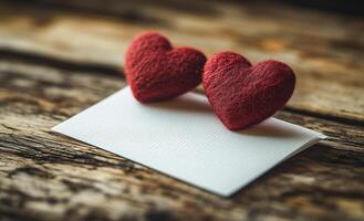 Two red hearts on a white card. The card is on a wooden surface. The hearts are placed on top of the card, and the card is empty photo