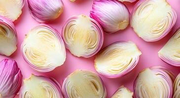 A close up of onion slices on a pink background. The onions are cut in half and arranged in a pattern photo
