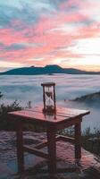 A wooden table with an hourglass on top of it overlooking the mountains photo