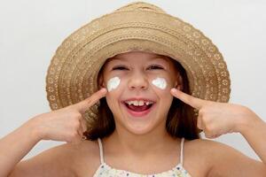 Portrait of caucasian smiling child in straw hat showing on cheeks with cream of 6 7 years looking at camera photo