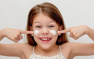 Portrait of caucasian smiling child showing on cheeks with cream of 6 7 years looking at camera photo