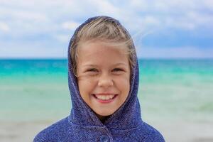 Portrait of smiling caucasian child 7 8 years in hood in windy weather on sea background looking at camera photo