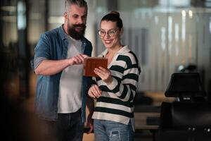 Male senior coach or speaker sharing business ideas and collaborating with a diverse team in a modern office, presenting a project on a tablet during a brainstorming session in a startup hallway photo