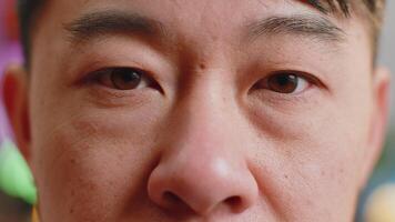 Close-up macro portrait of asian man face smiling, brown gauy eyes looking at camera blink wink video