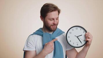 Smiling man showing time on wall office clock, ok, thumb up, approve, pointing finger at camera video