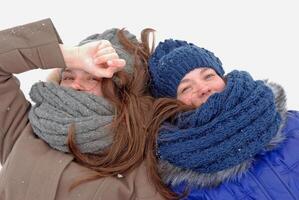 Two girls lying in the snow wearing scarves and hats photo