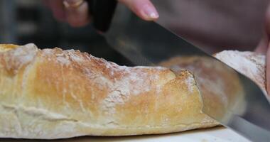 Baguette. French Baguette. Homemade bread loaf being sliced on a cutting board by the chef in a home kitchen. After baking in the oven. Cheese and wine in the background. Action shot. Hands and pans. video