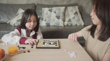 Asian family, mum, and kid fun playing Go, checkers board game on table in home living room together with love and cheerful, happy weekend relaxing hobby of child and parent, compete with concentrate. video