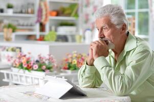 Elderly man posing at a table with a tablet photo