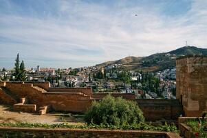 Elevated view of a historic European city Granada, Spain with white buildings, terracotta roofs, and lush green hills on Albaicin district in the background. Sunny day with clear blue skies photo