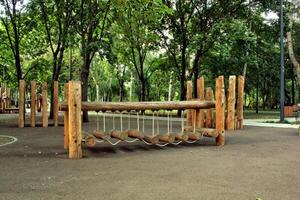 Wooden playground climbing frame with rope ladder and slide in a green park. Sunny day with trees in the background. Children's outdoor activity and recreation photo