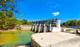 Scenic View of a Modern Dam Structure with Clear Blue Sky and Lush Greenery Surrounding a Tranquil River on a Sunny Day photo