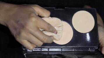Close-up shot features a hand applying makeup with a sponge from a palette. Enhancing beauty through cosmetics, face make-up products. video
