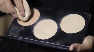 Close-up of a woman applying face powder with a powder puff from a palette. She is using different shades to contour her face. video