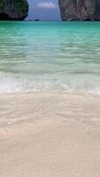 a beach with clear water and a large rock on Phi Phi beach. video